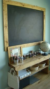 a blackboard mounted to the side of a wall above a wooden shelf with baskets on it