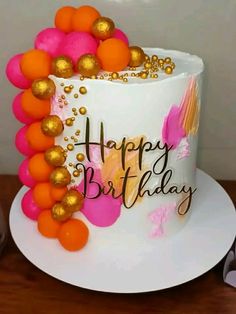 a birthday cake decorated with orange and pink balloons on a white plate next to a pair of glasses