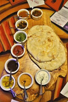 a wooden table topped with lots of different bowls and sauces next to an uncooked pita bread