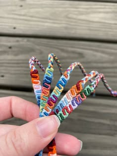 a hand is holding a small multicolored beaded object in front of a wooden background