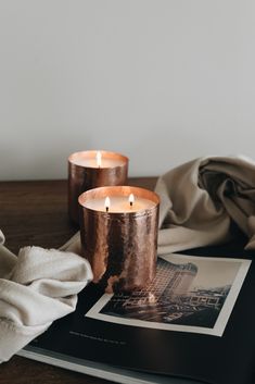 two candles sitting on top of a table next to an open book and white cloth