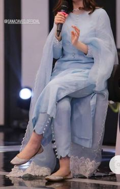 a woman sitting on top of a chair with a microphone in her hand and wearing a blue outfit