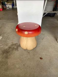 a red and yellow mushroom sitting on top of a wooden stool in a garage area