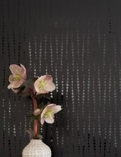 a white vase with flowers in it sitting on a table next to a black wall