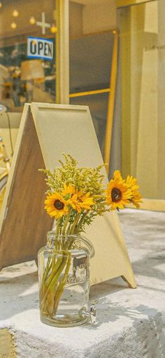 a vase filled with yellow flowers sitting on top of a table next to a sign