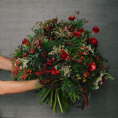 a woman holding a bouquet of red flowers and greenery with her hands on it