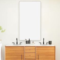 a bathroom vanity with two sinks and a large mirror above it, in front of a white wall