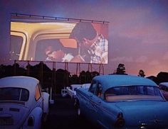 two cars parked next to each other in front of a large screen