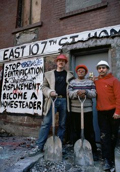 three men standing in front of a building with shovels and signs on the wall