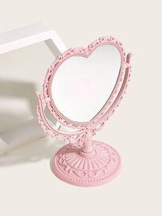 a pink heart shaped mirror sitting on top of a white table next to a box