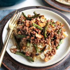 a white plate topped with rice covered in meat and veggies next to a fork