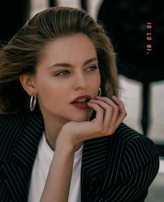 a woman in a pinstripe jacket is posing with her hand on her chin