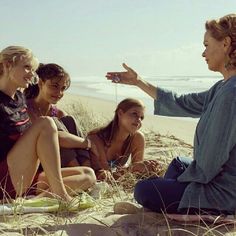 a group of women sitting on top of a sandy beach next to the ocean talking