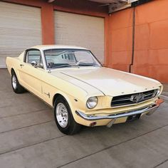 an old yellow mustang parked in front of a garage