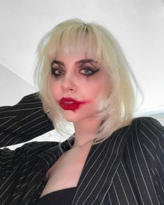 a woman with white hair wearing a black and white striped blazer, red lipstick, and dark eyeliners