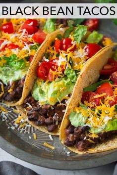 three tacos with lettuce, tomatoes, black beans and cheese on a plate