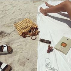 a woman laying on top of a white towel next to sandals and an open book