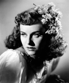 an old black and white photo of a woman with flowers in her hair, looking to the side