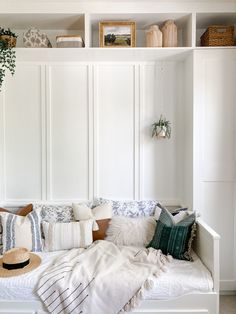 a white couch with pillows and blankets on top of it in front of some shelves