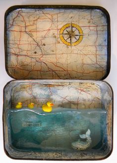 an open suitcase with yellow rubber ducks in the water and a compass on it's lid