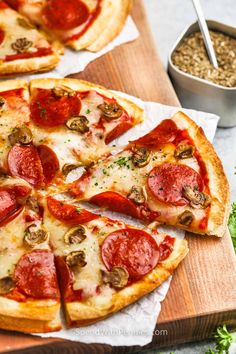 two pizzas with pepperoni and mushrooms are on a cutting board next to a bowl of seasoning