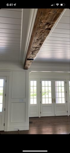 an empty room with white doors and wood beams on the ceiling, and windows in the wall