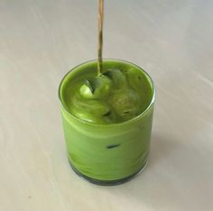 a green cup filled with liquid sitting on top of a white table next to a wooden stick