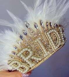 a hand holding a tiara with pearls and feathers