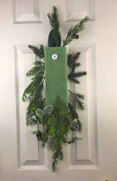 a green door hanger decorated with evergreens and pineconi leaves on a white front door