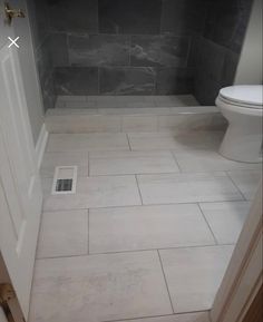 a white toilet sitting inside of a bathroom next to a walk in shower door and tiled floor