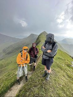 three people hiking up a grassy hill with mountains in the background