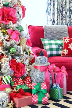 a christmas tree with presents under it in front of a red couch and checkered rug