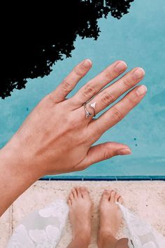 a person's hand with a ring on their finger next to a swimming pool