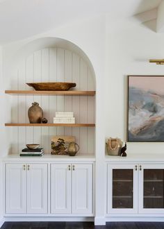 a room with white cabinets and bookshelves on top of each other in front of a painting