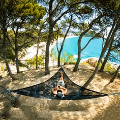 a person laying in a hammock on the ground next to some trees and water