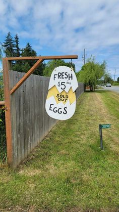 a sign for fresh eggs on the side of a road in front of a fence