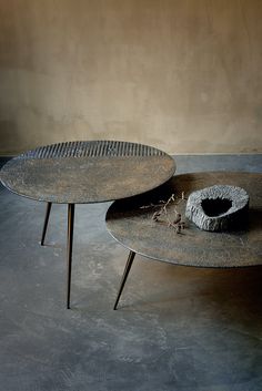 two round tables sitting on top of each other in front of a wall with a vase