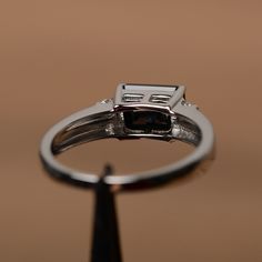 It is a black spinel ring. The main stone is 6mm*8mm emerald cut, weight about 1.80 carats. The basic metal is sterling silver and plated with rhodium. To change the metal to a solid gold (white/rose) or platinum is also available, please ask for a quotation if you want. You can also go to my shop Home for more elegant rings: https://www.etsy.com/shop/godjewelry?ref=hdr_shop_menu More black spinel rings: https://www.etsy.com/shop/godjewelry?ref=seller-platform-mcnav§ion_id=21680005 Customization Classic Black Baguette Cut Rings, Black Baguette Cut Ring For Formal Occasions, Formal Black Baguette Cut Rings, Black Diamond Ring With Prong Setting In Emerald Cut, Black Emerald Cut Promise Ring, Black Emerald Cut Diamond Ring For Promise, Black Emerald Cut Diamond Promise Ring, Black Emerald Cut Diamond Anniversary Ring, Silver Solitaire Engagement Ring