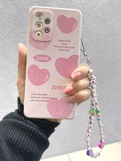 a person holding up a pink phone case with hearts on it and a keychain attached to the back