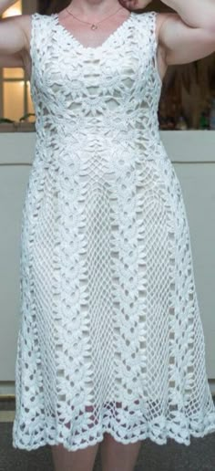 a woman wearing a white crochet dress and holding her hands behind her head