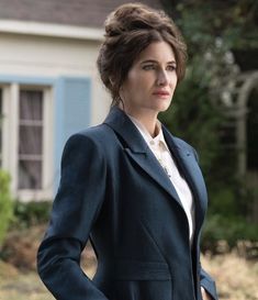 a woman standing in front of a house with her hands on her hips and looking at the camera