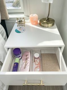 an open drawer in a white dresser next to a lamp