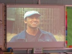 there is a man that is smiling on the screen in front of his class room