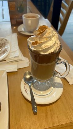 a cappuccino with whipped cream on top sits on a table next to a cup of coffee