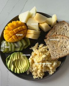 a black plate topped with sliced up fruit and bread on top of a white table