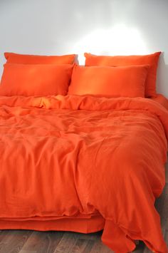 an orange comforter and pillows on a bed in a room with wood flooring