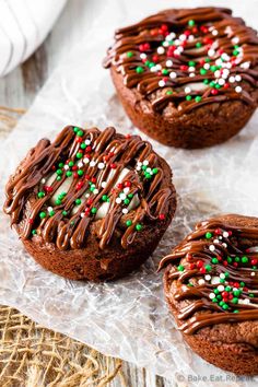 three cookies with chocolate frosting and sprinkles on top of some wax paper