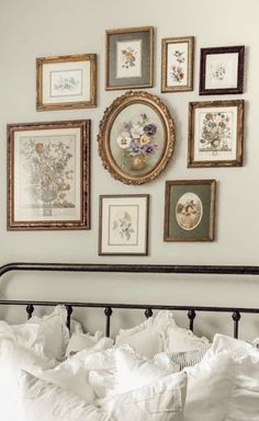 a bed with white linens and framed pictures on the wall above it in a bedroom