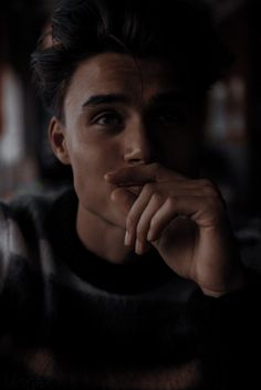 a man with his hand on his chin looking at the camera while sitting in a dark room