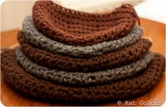 a stack of crocheted hats sitting on top of a wooden table next to a white cat